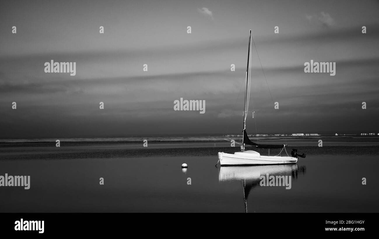 Un paysage noir et blanc d'un voilier au repos dans une baie sous un ciel couvert Banque D'Images