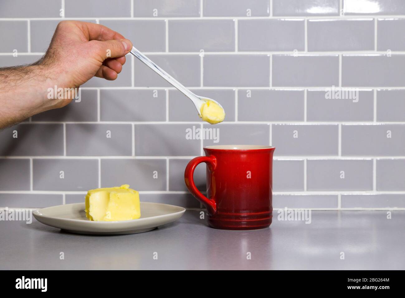 Main du Mans tenant une cuillère à café de beurre avec un mug à café rouge pour faire du café à l'épreuve des balles. Banque D'Images