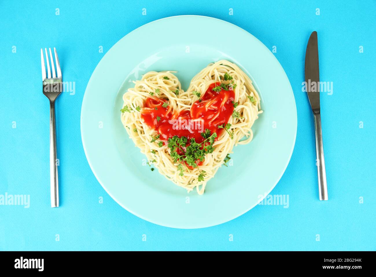 Spaghetti cuit soigneusement arrangé en forme de coeur et recouvert de sauce tomate, sur fond de couleur Banque D'Images