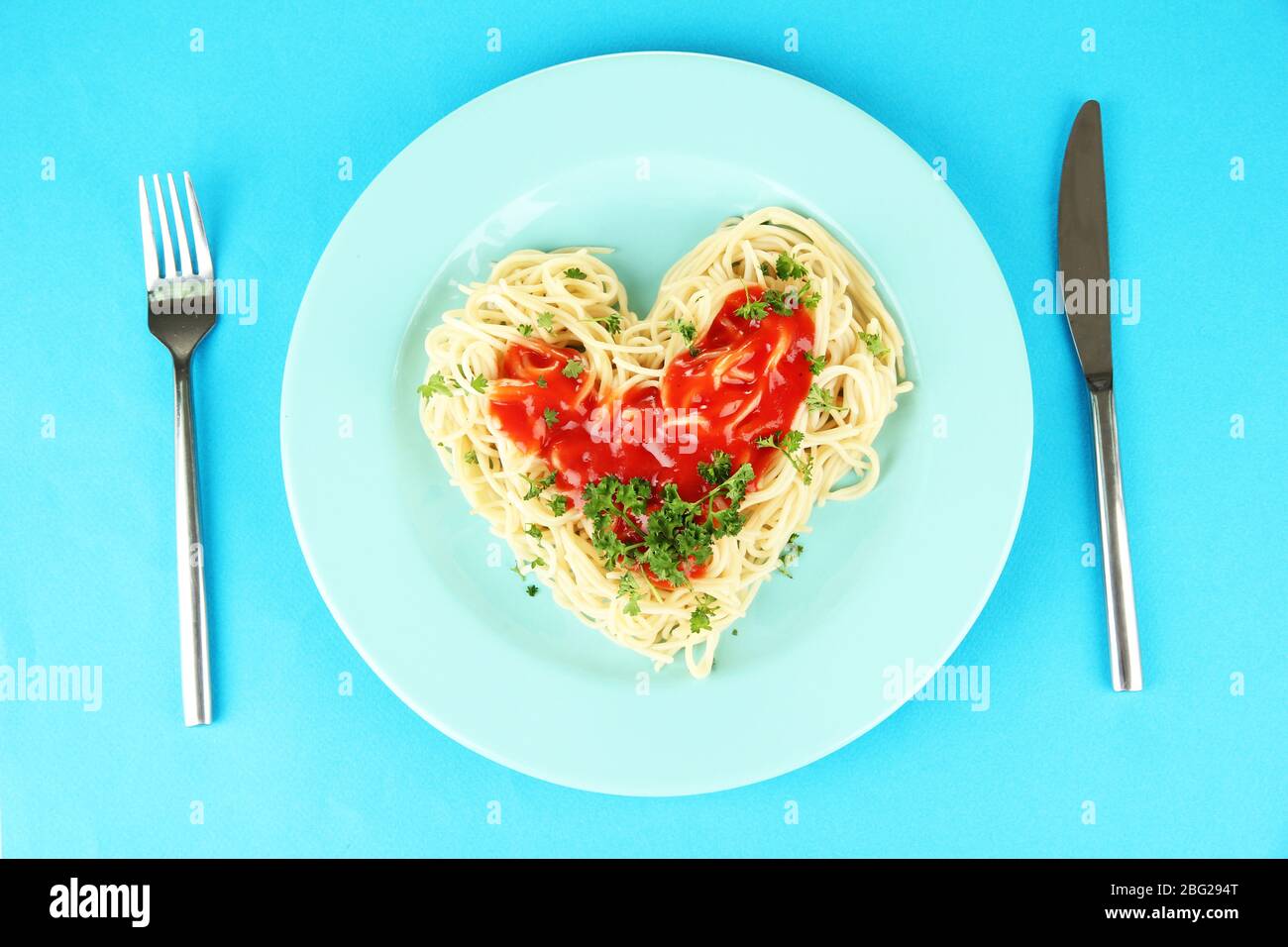 Spaghetti cuit soigneusement arrangé en forme de coeur et recouvert de sauce tomate, sur fond de couleur Banque D'Images