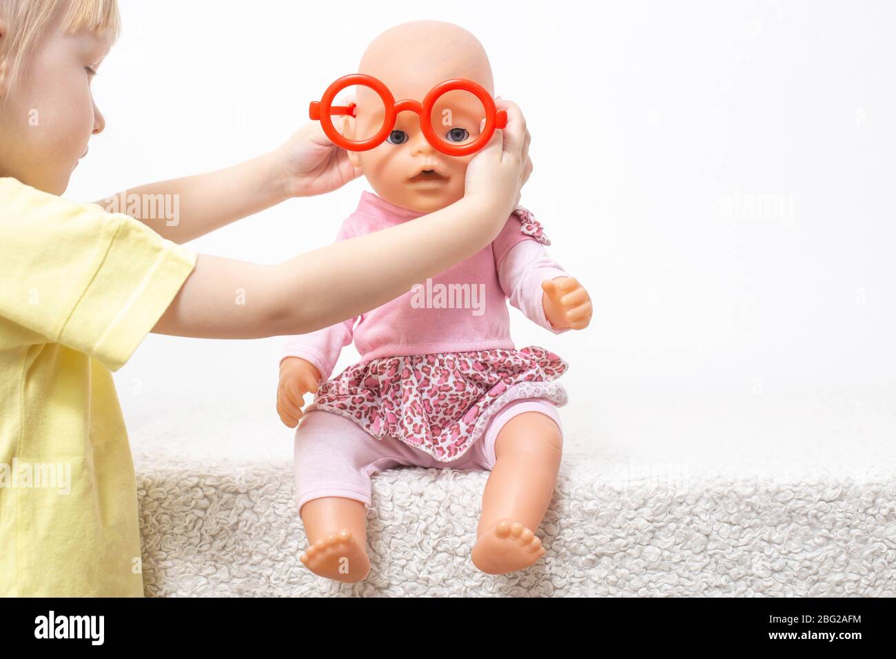 L'enfant joue avec une poupée et met sur des lunettes de jouet. Le concept  de l'ophtalmologie pédiatrique, la sélection de lunettes et le traitement  de la déficience visuelle i Photo Stock -