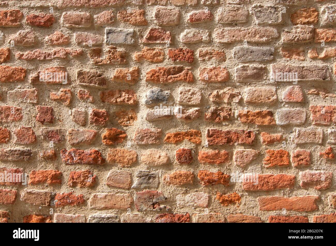 Ancienne texture de fond de mur de brique avec différentes teintes de rouge et différentes formes de pierre, illuminée par le soleil Banque D'Images