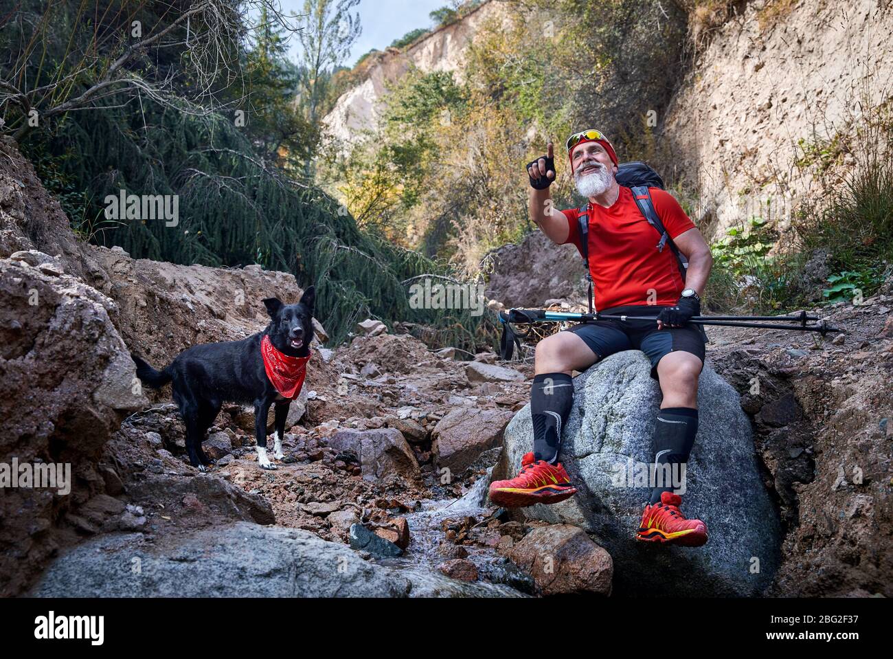 Homme barbu en chemise rouge avec chien près de la rivière dans la forêt. Outdoor travel concept Banque D'Images