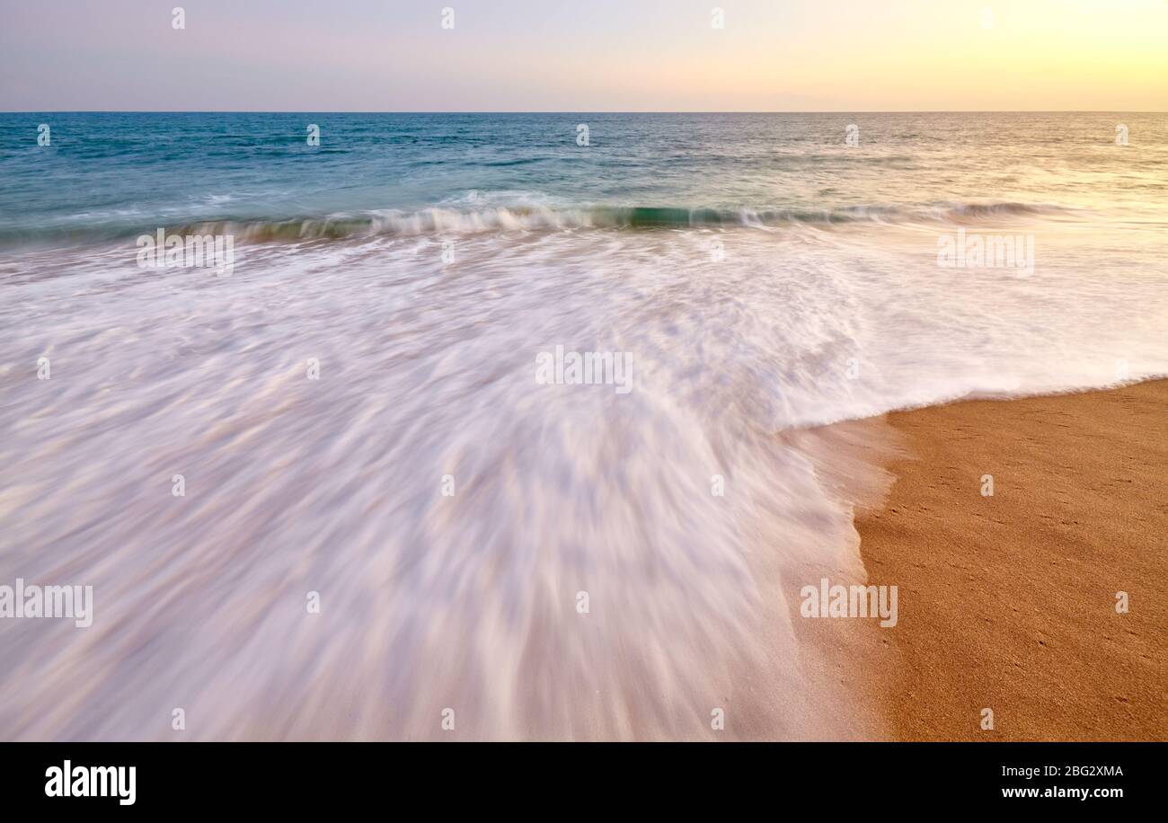 Mouvement vague floue entrant sur la plage de sable au coucher du soleil. Banque D'Images