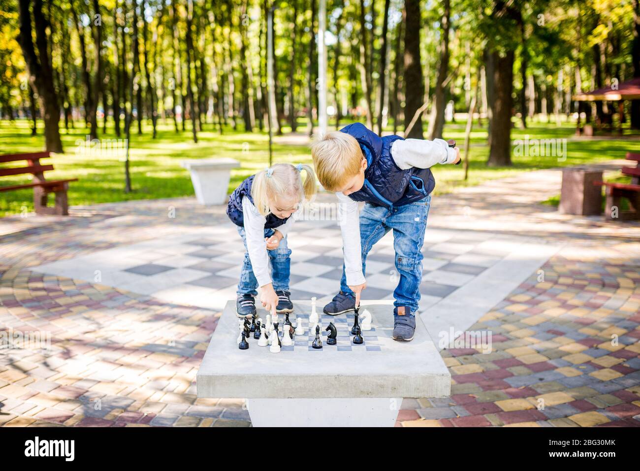 Passe-temps des enfants, des garçons et des filles jouant aux échecs. Drôle petit frère et soeur jouant aux échecs en plein air dans le parc sur un site public. Enfants de club de loisirs Banque D'Images