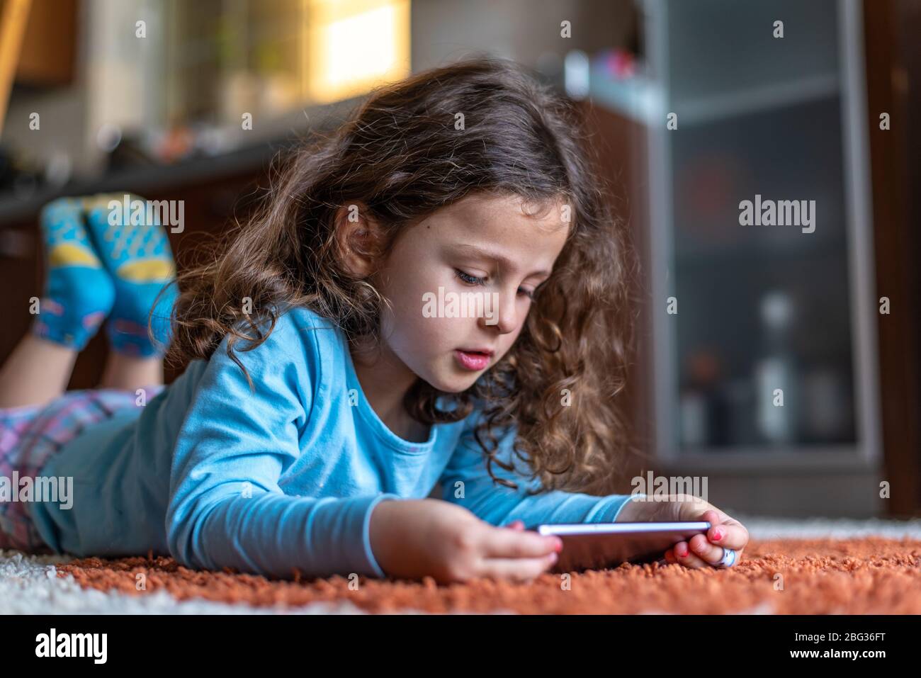 Jolie petite fille heureuse posée sur l'utilisation de smartphone numérique mobile dans le salon à la maison. Concept d'activité familiale. Banque D'Images