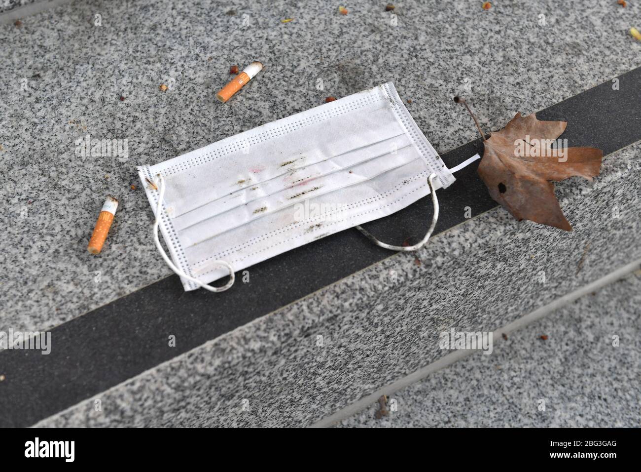 Munich, Allemagne. 20 avril 2020. Crise de Corona: La simple protection du nez de bouche se trouve sur un escalier en pierre à côté d'un bout de cigarette après qu'il a été jeté loin. Masque jetable, déchets. | utilisation dans le monde crédit: dpa/Alay Live News Banque D'Images