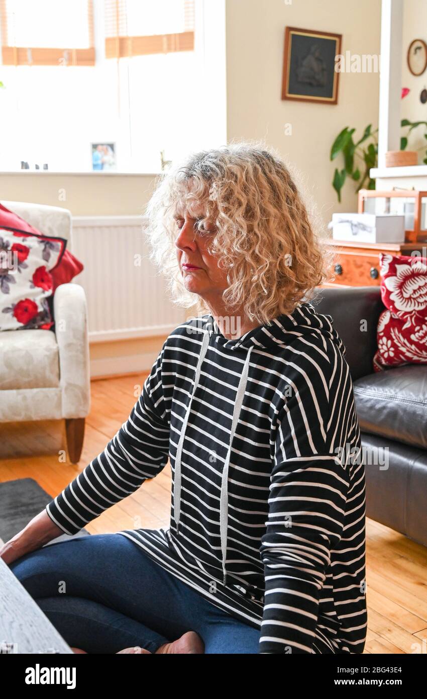 Une femme d'âge moyen mûre faisant des exercices de relaxation et de respiration à la maison en regardant une leçon sur son smartphone Banque D'Images