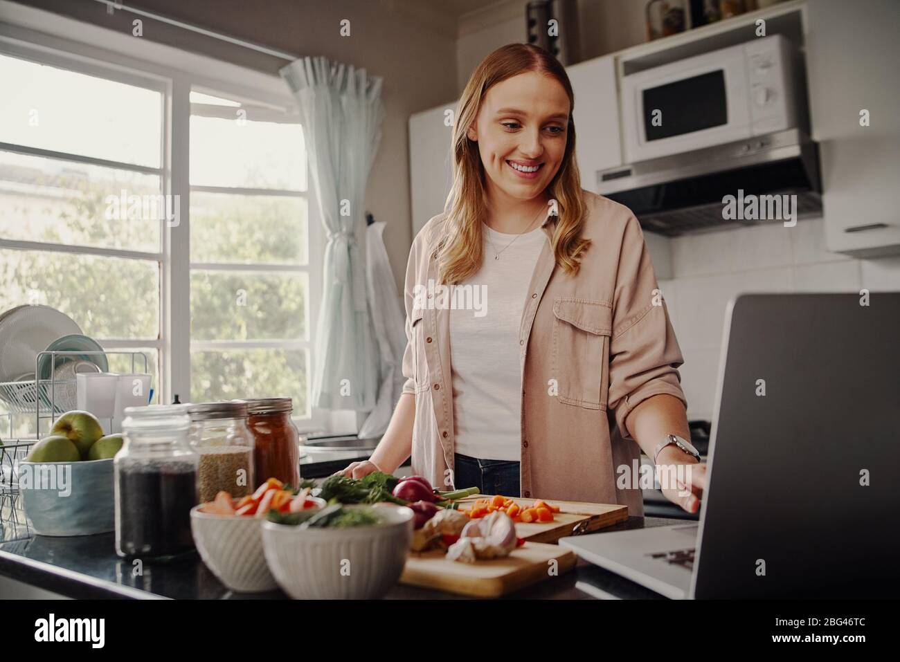 Jeune femme gaie blogger de la navigation pour la recette en ligne pour préparer la salade de légumes frais et de poste sur les médias sociaux dans vlog Banque D'Images