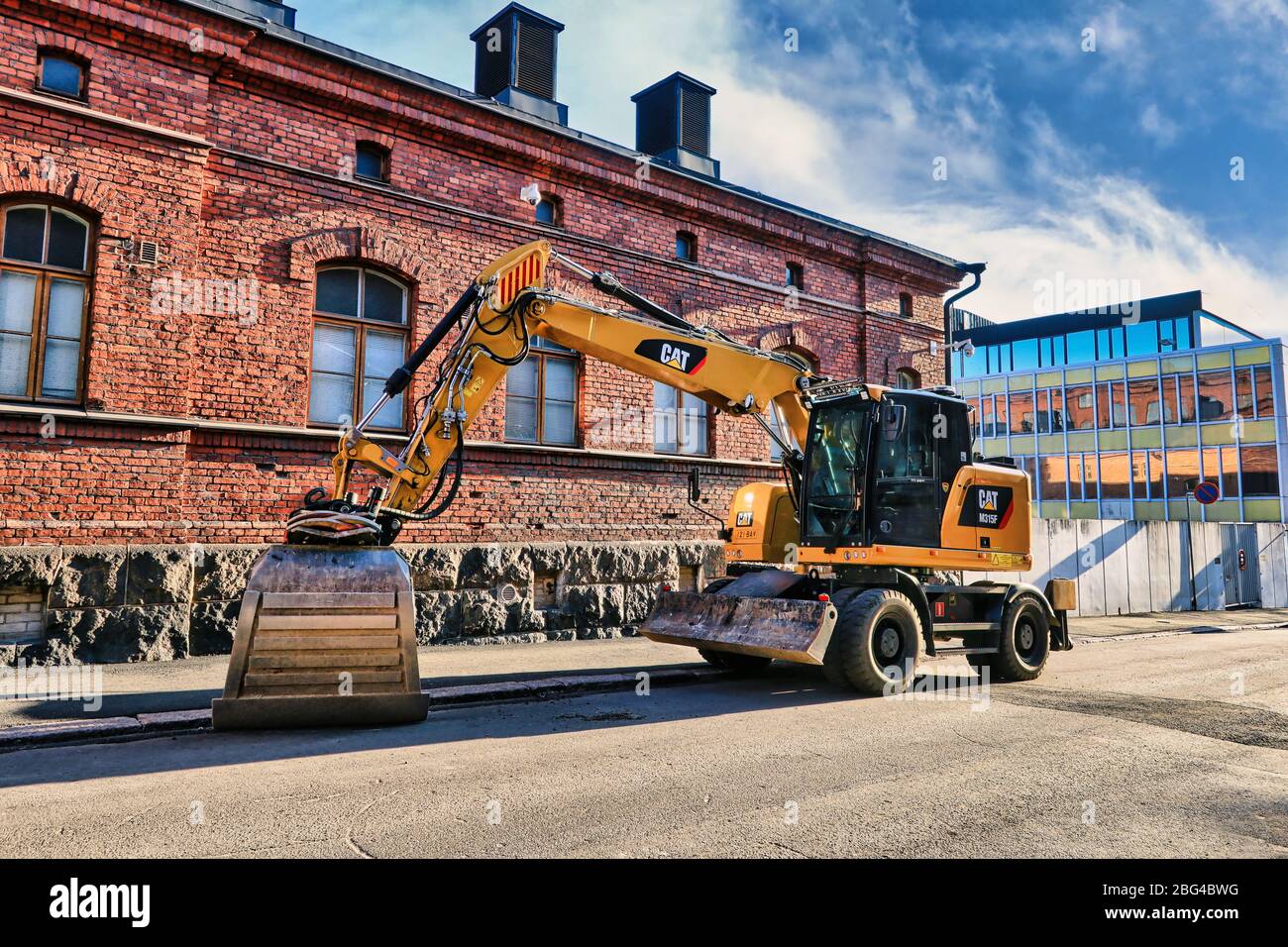 Nouvelle pelle hydraulique sur pneus M315 F Cat stationnée sur une allée à côté du bâtiment historique en brique rouge à partir de la ville de 1889. Helsinki, Finlande. 19 avril 2020. Banque D'Images