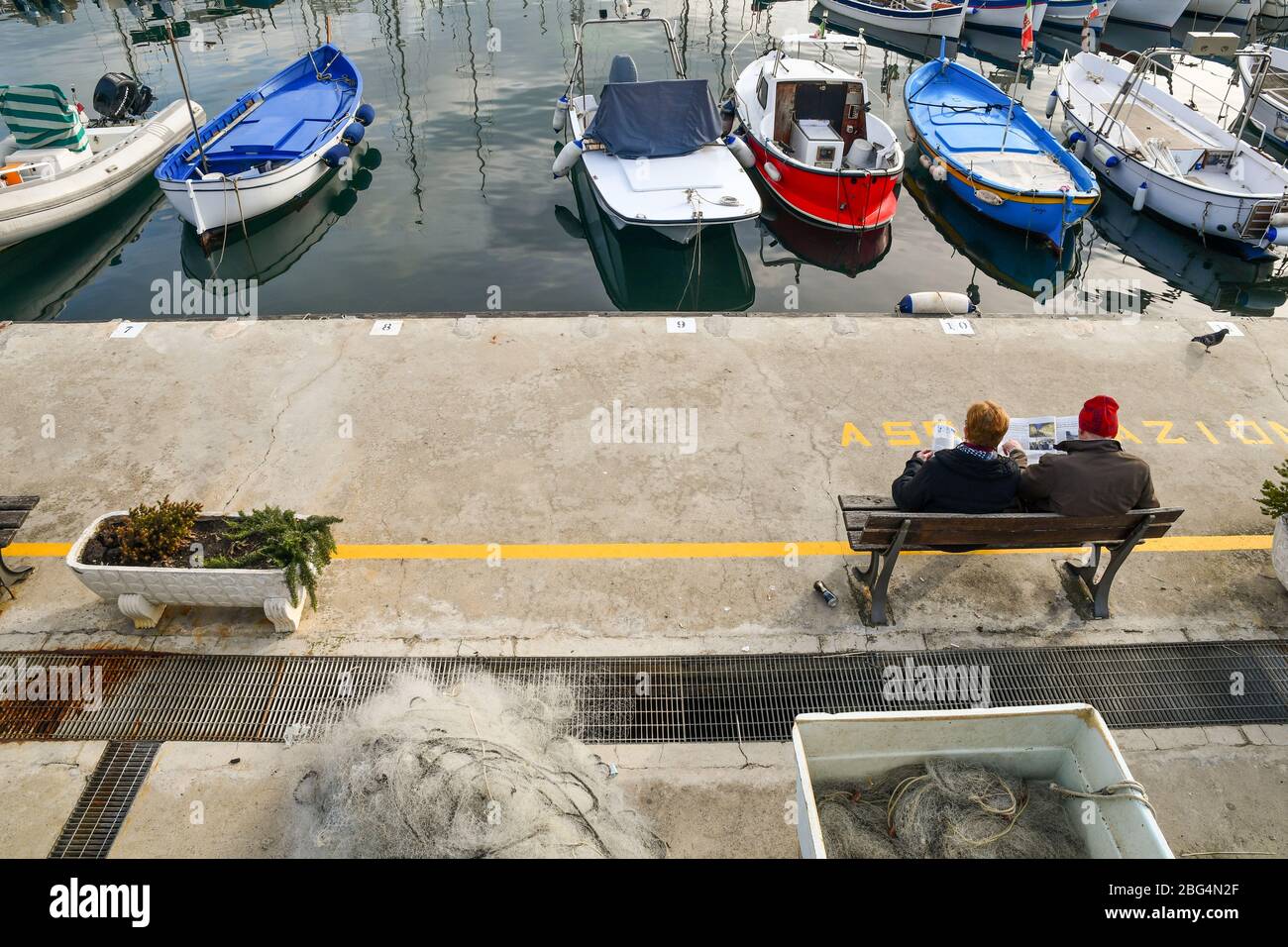 Vue panoramique sur un couple âgé assis sur un banc et lisant des journaux sur le quai du port en hiver ensoleillé, Sanremo, Ligurie Italie Banque D'Images