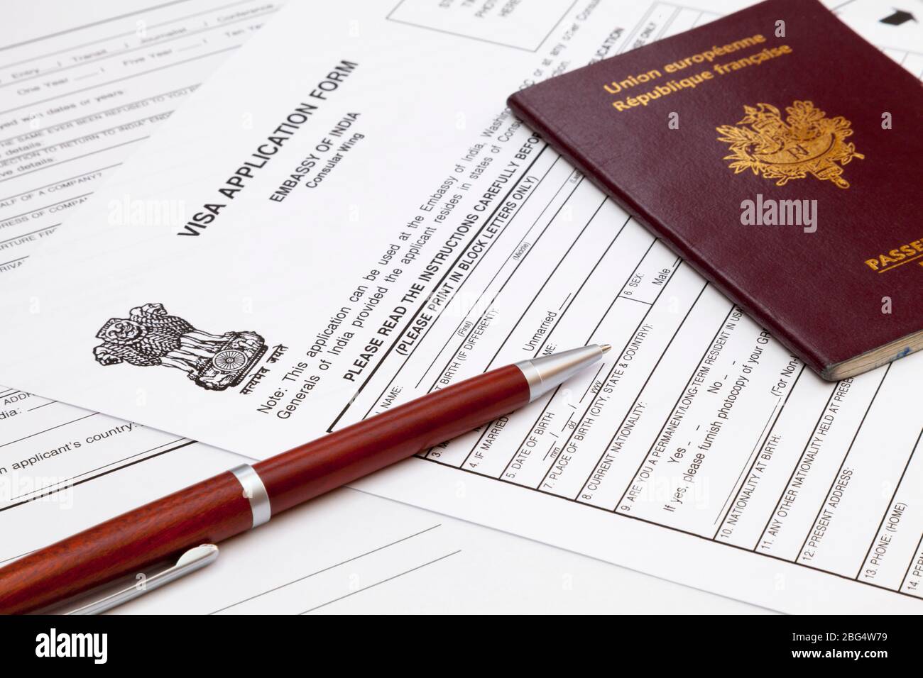 Un stylo bille et un passeport français sur le dessus d'un formulaire de demande de visa indien. Banque D'Images