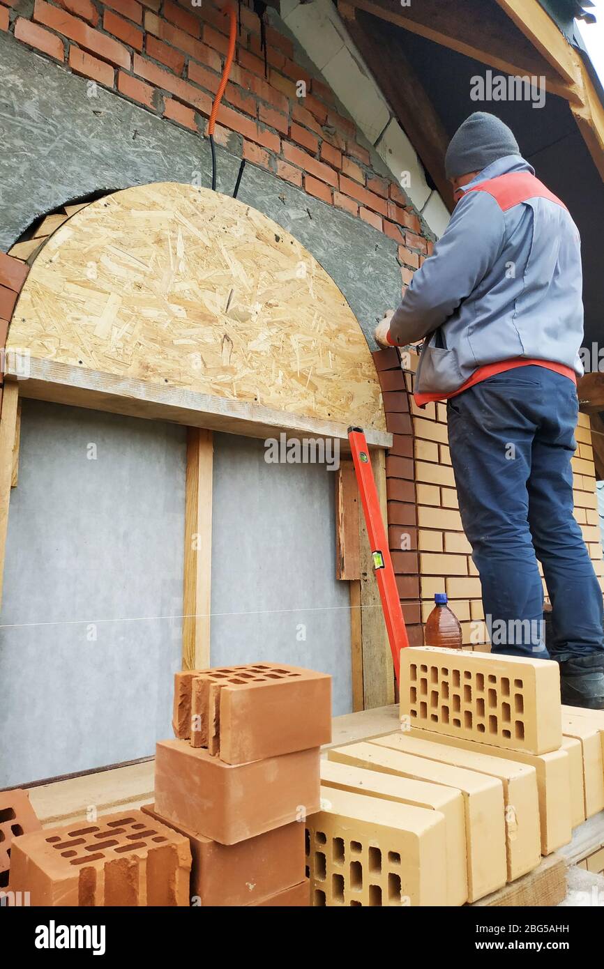 Le maître dans une combinaison bleue construit un mur de face brique.2020 Banque D'Images