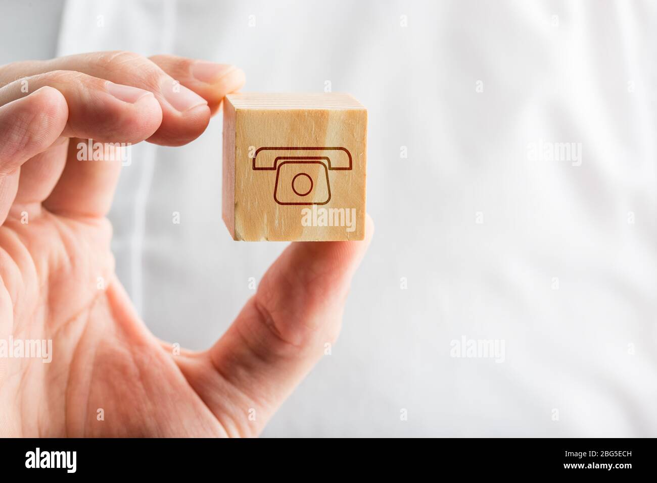 Homme tenant une icône de téléphone sur un cube en bois dans sa main conceptuel des télécommunications, contact, assistance, chat et soutien client. Banque D'Images