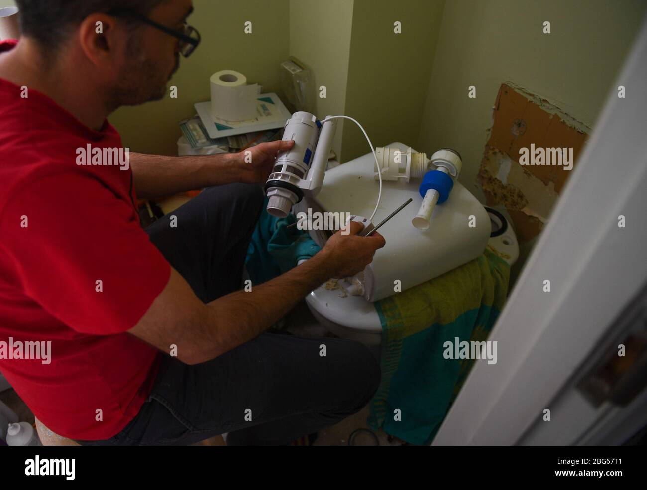 Verrouillage du bricolage, UN homme fixe un mécanisme de rinçage de toilettes en le remplaçant par une nouvelle unité. Banque D'Images