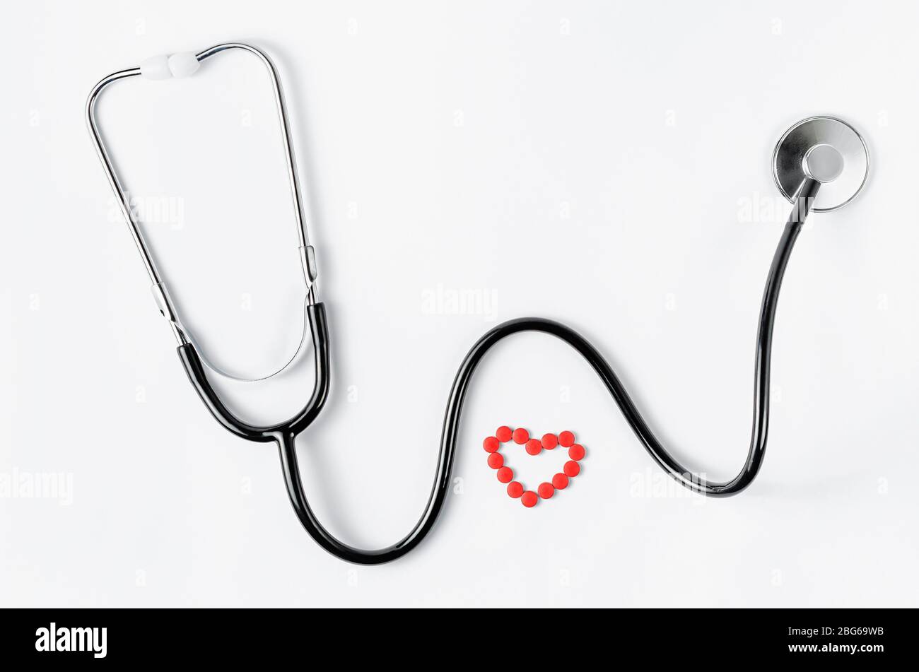 Système cardiovasculaire. Stéthoscope et pilules rouges en forme de coeur sur fond blanc. Espace de copie. Vue de dessus Banque D'Images