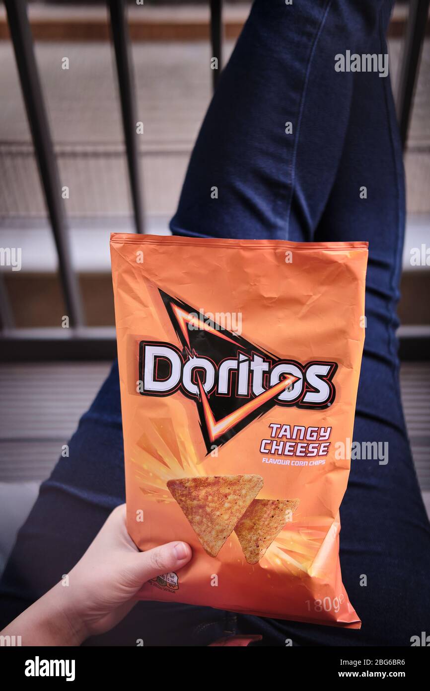 Les womans ont croisé les jambes en Jean bleu avec une main tenant un paquet orange de fromage acidulé doritos sur ses genoux Banque D'Images