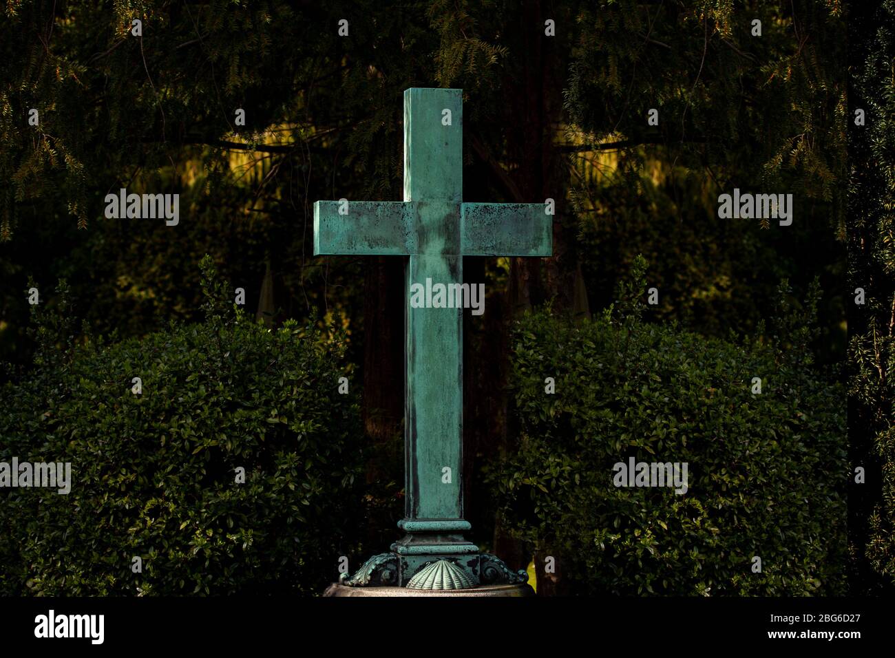 Croix verte chrétienne blanche verdigrisée dans un cimetière avec feuillage vert avec espace de copie. Symbole pour le christianisme, la résurrection et Jésus-Christ. Banque D'Images