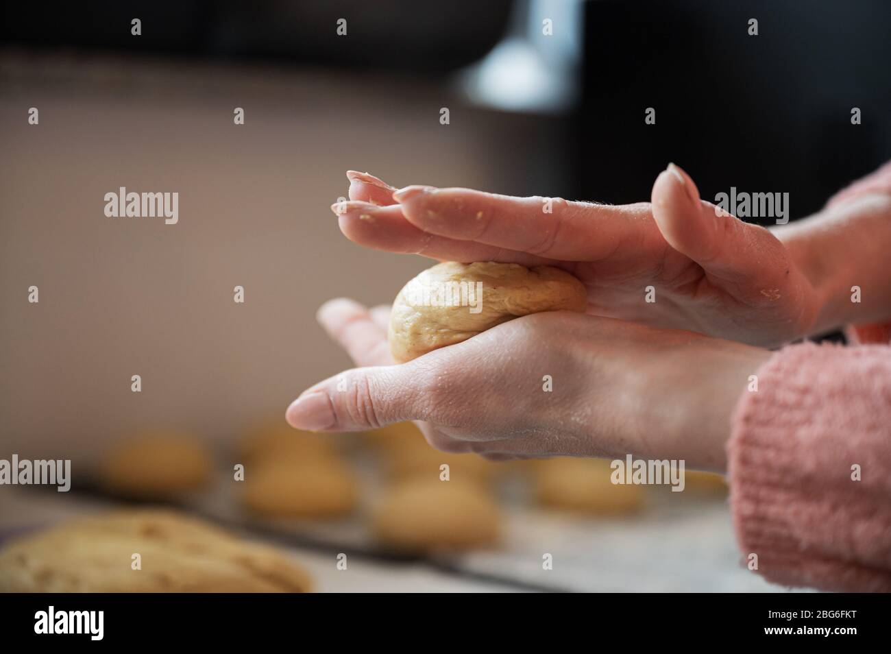 Vue rapprochée des mains féminines façonnant du pain ou des boules de beignet à partir de la pâte végétalienne. Banque D'Images