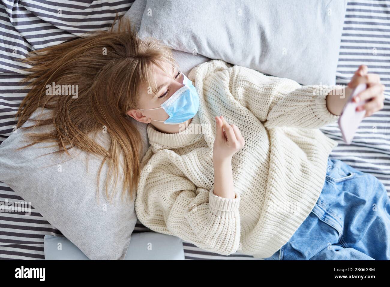 Jeune adolescent dans le masque médical allongé sur un lit et faisant un  appel vidéo montrant le coeur coréen. Cœur coréen - geste de la pointe du  pouce et de l'index Photo