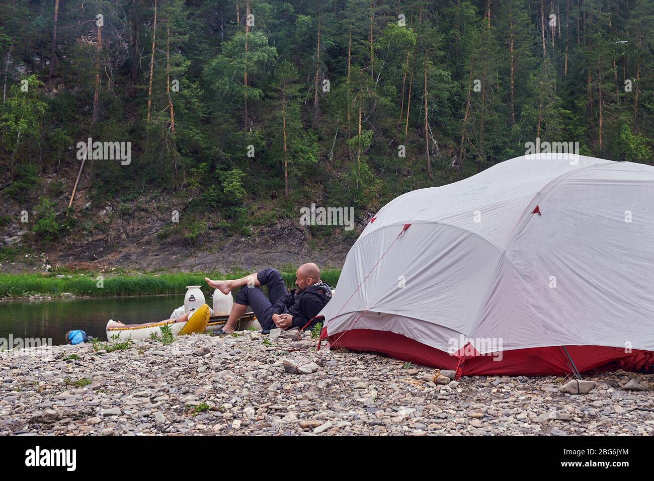 Un jeune homme barbu boit du thé lors d'un voyage de camping, dans la nature, en toile de fond d'une tente touristique. Banque D'Images