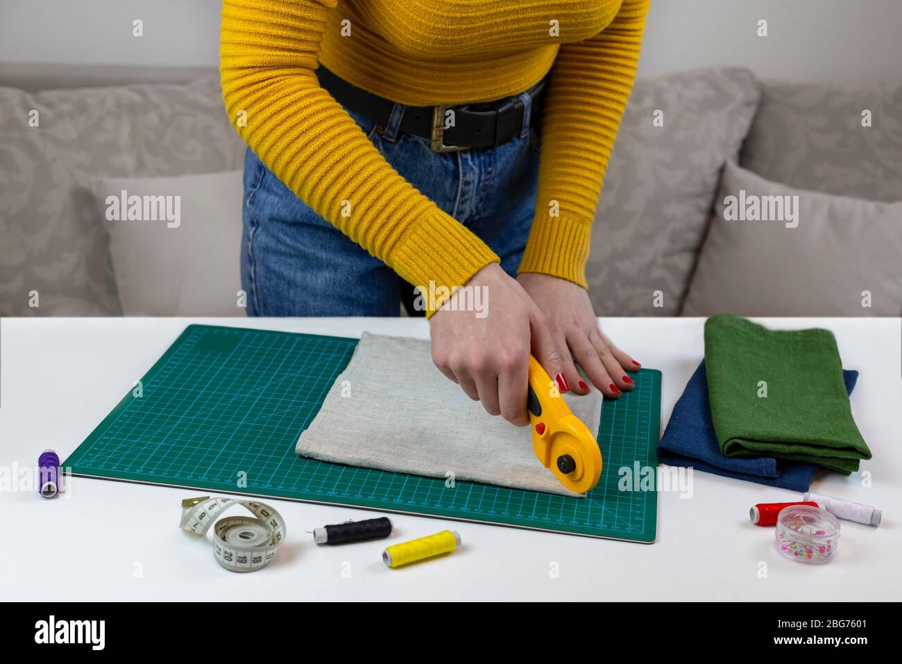 femme dans un tissu de découpe jaune. il y a des outils de courtepointes sur la table. couteau patchwork, ciseaux, tapis de coupe doublé, auto-verrouillage, filetage, centimet Banque D'Images femme dans un tissu de découpe jaune. il y a des outils de courtepointes sur la table. couteau patchwork, ciseaux, tapis de coupe doublé, auto-verrouillage, filetage, centimet Banque D'Images