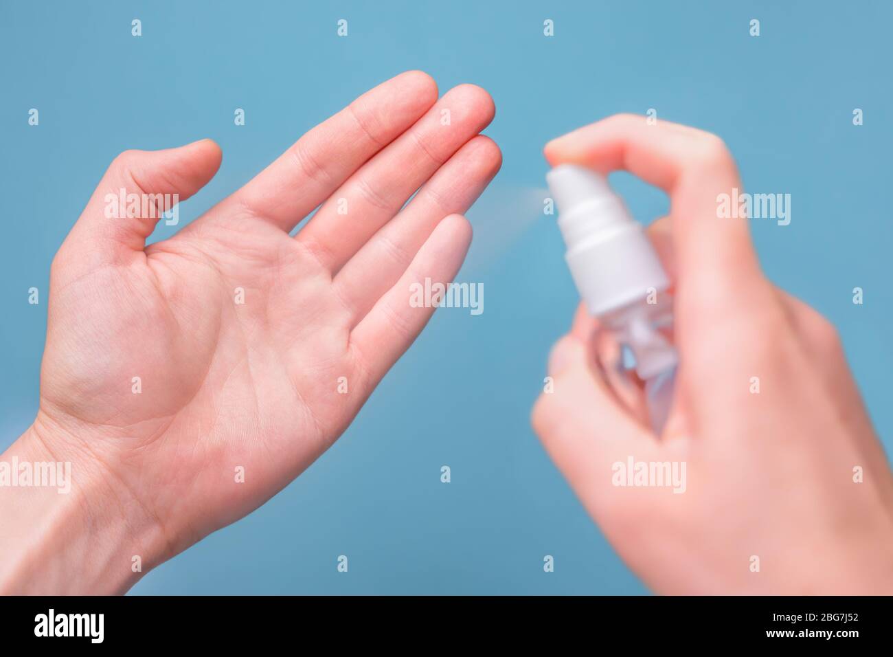 Mains vaporiser du désinfectant pour nettoyer et protéger les mains contre les virus sur fond bleu. Gros plan sur le smartphone désinfectant des mains. Nettoyez les mains avec Banque D'Images