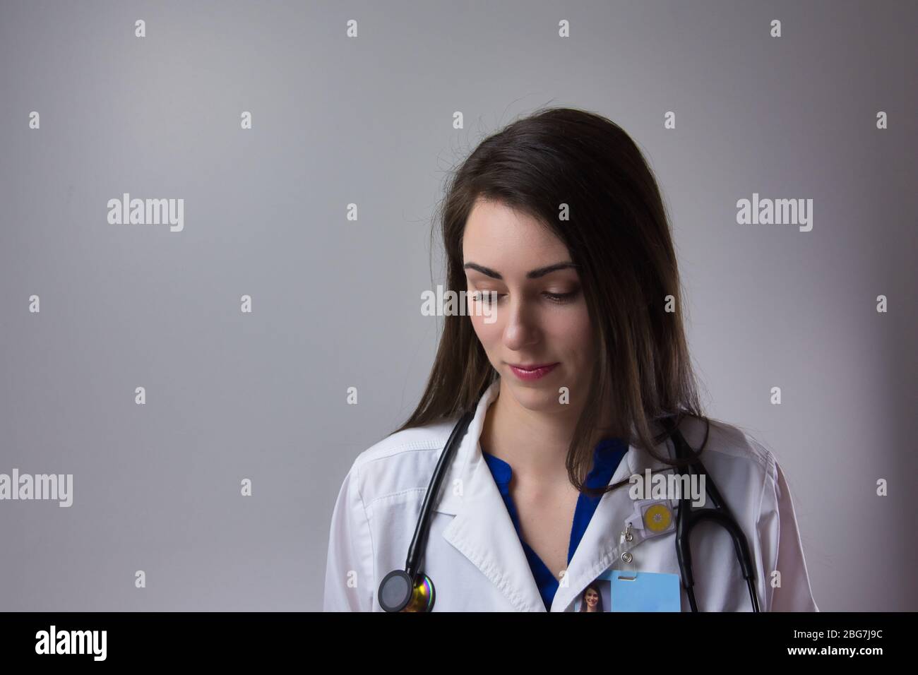 Médecin femme regardant vers le bas sur fond gris. Portrait isolé avec stéthoscope et badge Banque D'Images