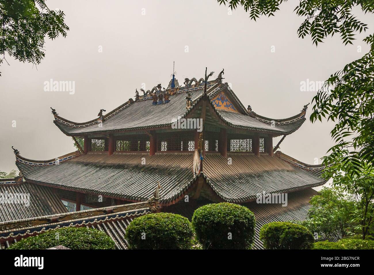 Fengdu, Chine - 8 mai 2010 : Ville fantôme, sanctuaire historique. Caractéristiques architecturales du toit chinois brun humide sous le ciel de pluie avec le feuillage vert. Banque D'Images