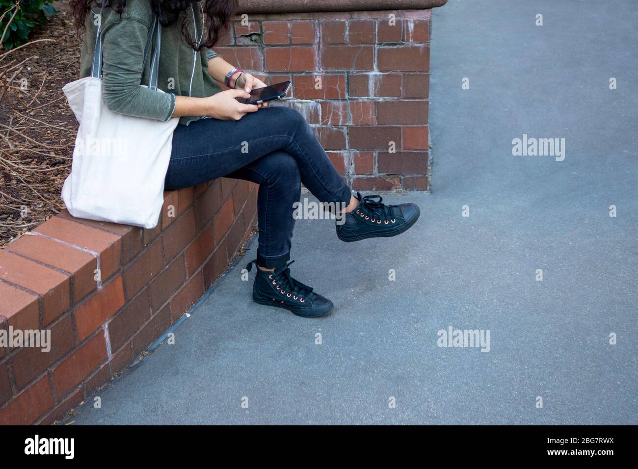 Jeune femme assise à l'aide d'un trottoir de téléphone mobile Banque D'Images