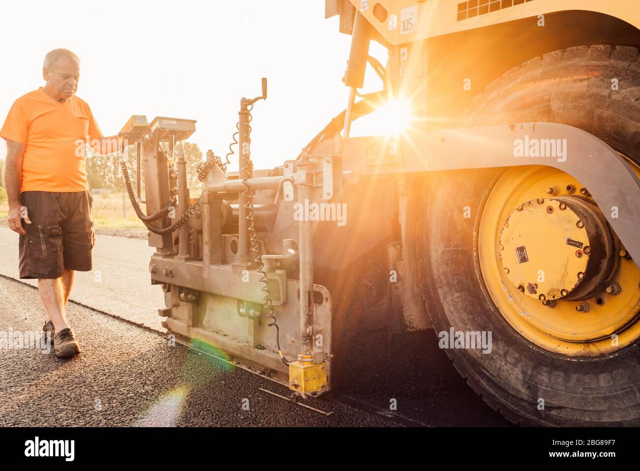 Travailleur routier exploitant une machine à asphalte qui pond de l'asphalte ou du bitume neuf pendant la construction de routes Banque D'Images