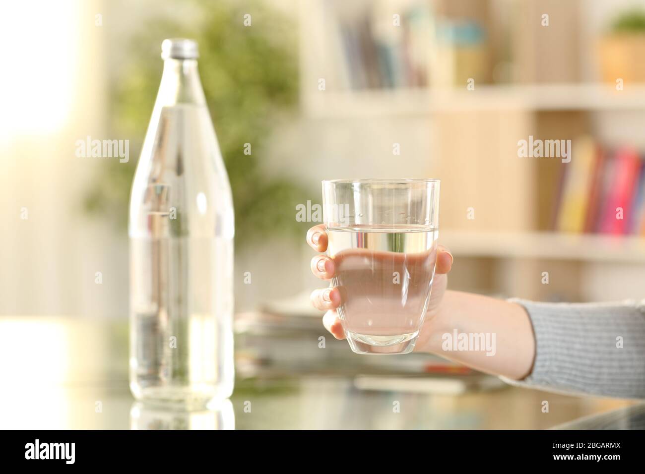 Gros plan sur les mains d'une femme tenant un verre d'eau en bouteille à la maison Banque D'Images