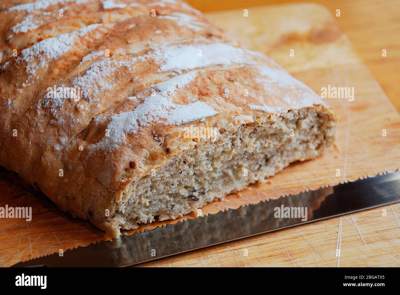 Un pain maison au levain sur une planche à découper en bois sur une table en bois avec un grand couteau à poignée noire dans un éclairage naturel Banque D'Images