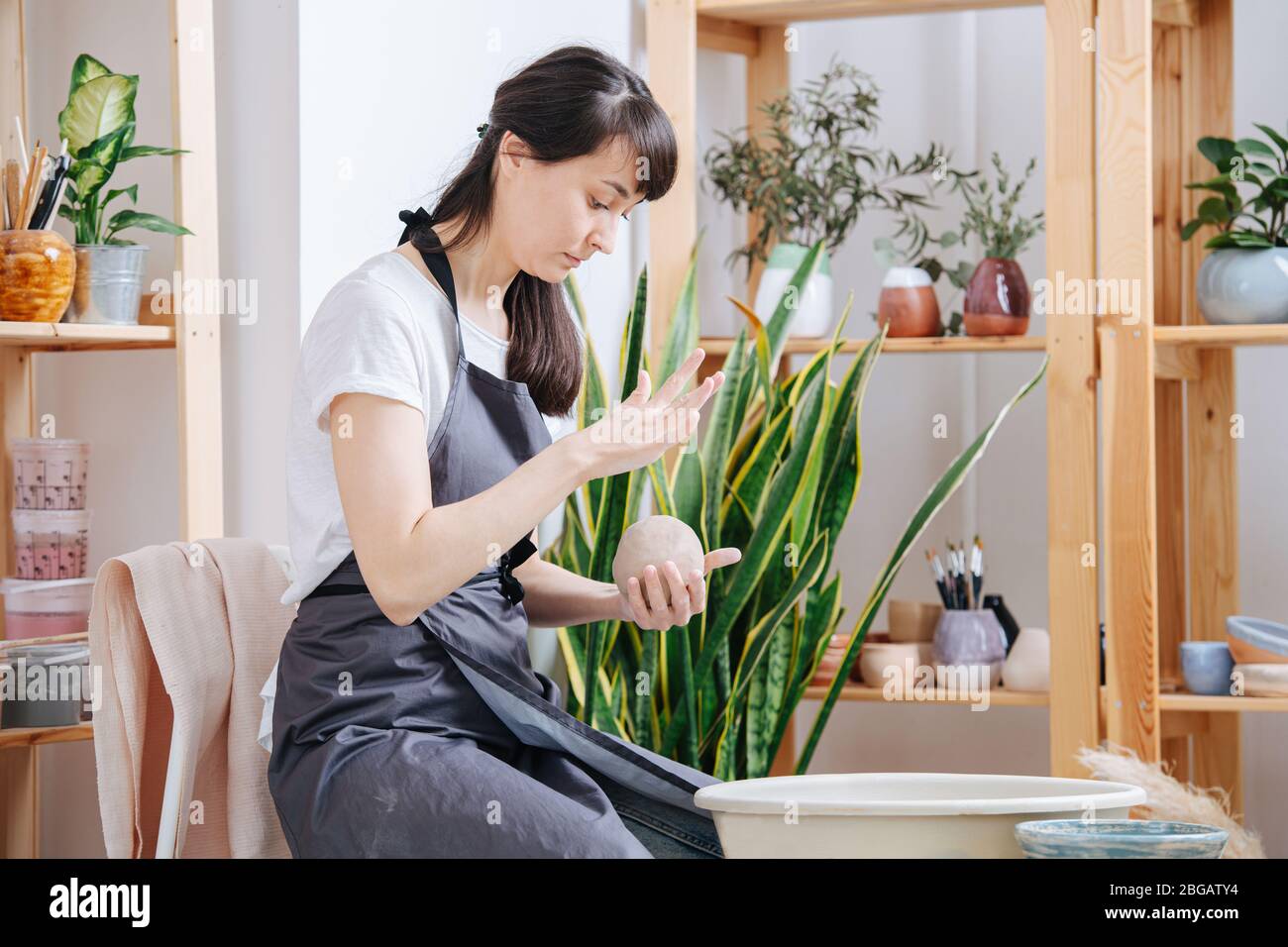 Femme travaillant avec de l'argile à côté d'une roue de poterie pour les futures céramiques Banque D'Images