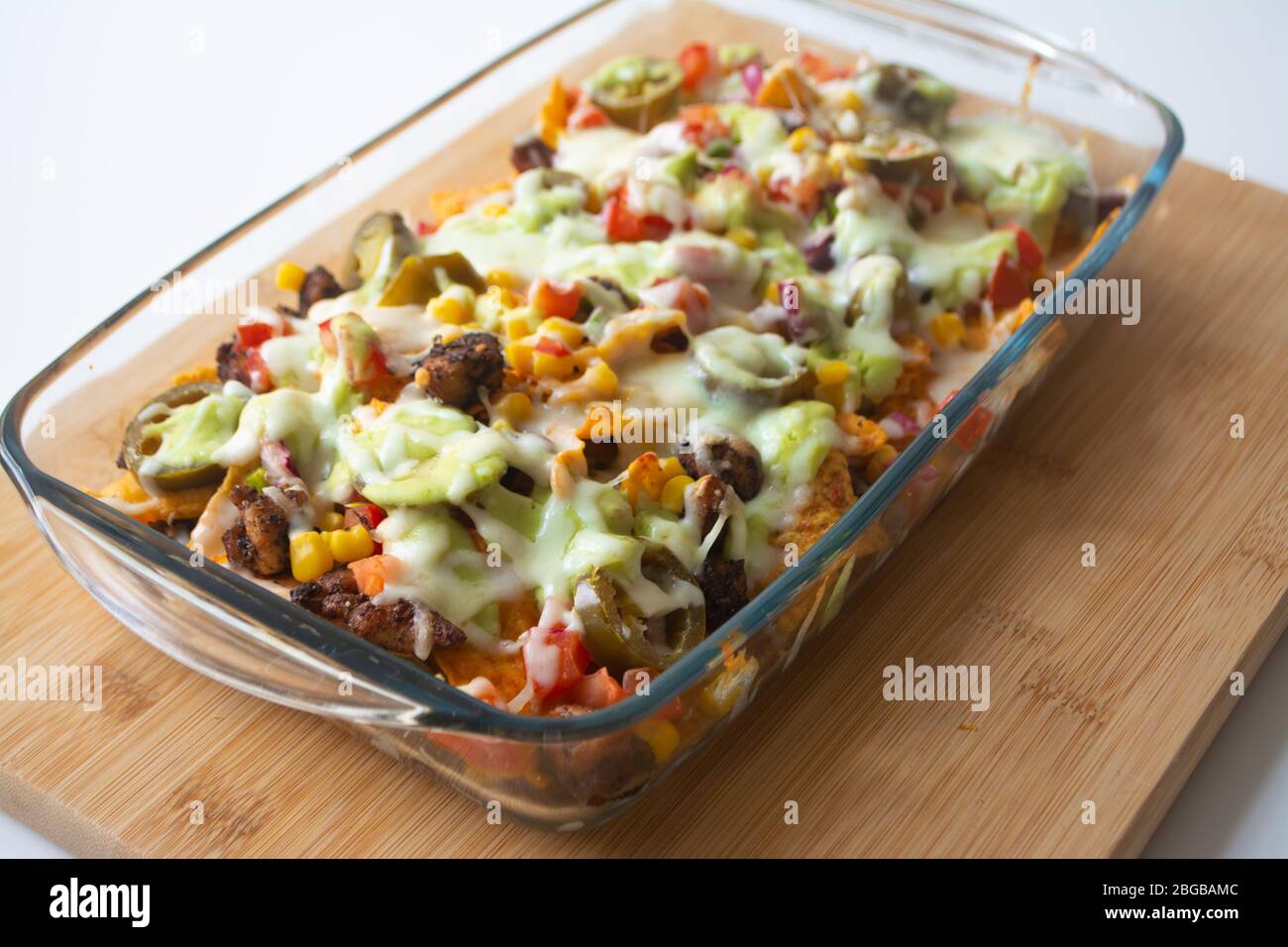 Nachos cuits au four avec chips de tortilla de maïs, maïs, guacamole, pico de gallo, haricots, jalapenos et Monterrey Jack dans un plat de cuisson en verre Banque D'Images