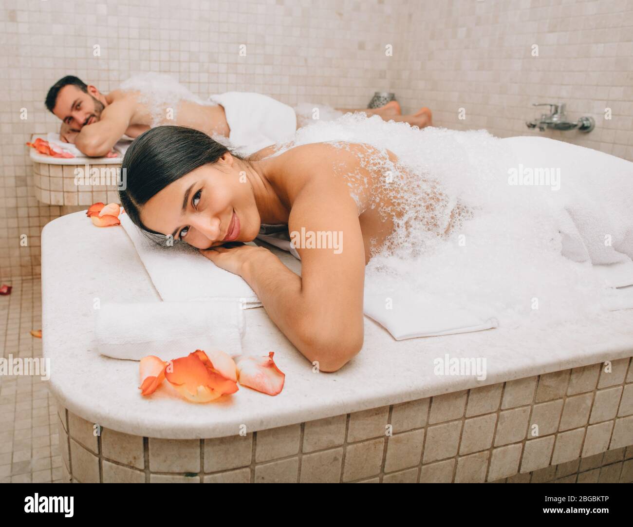 Belle femme et son petit ami se trouvent sur des tables de massage au hammam chaud avant les procédures de lavage du corps. Bain turc pour couple Banque D'Images