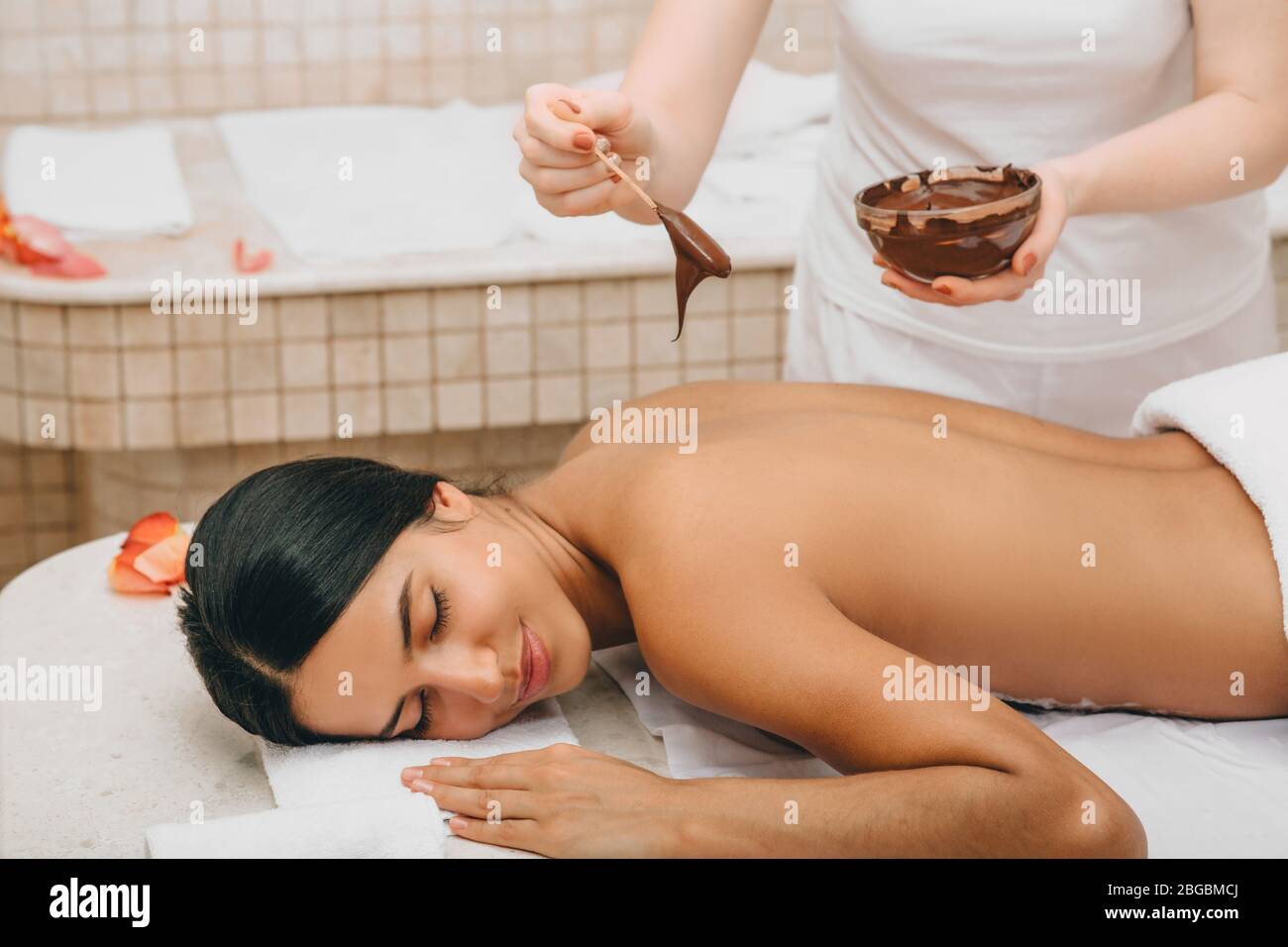 Femme mixte de course avec masque de corps en chocolat dans le salon de spa. Complexe de luxe et massage. Gommage au chocolat Banque D'Images