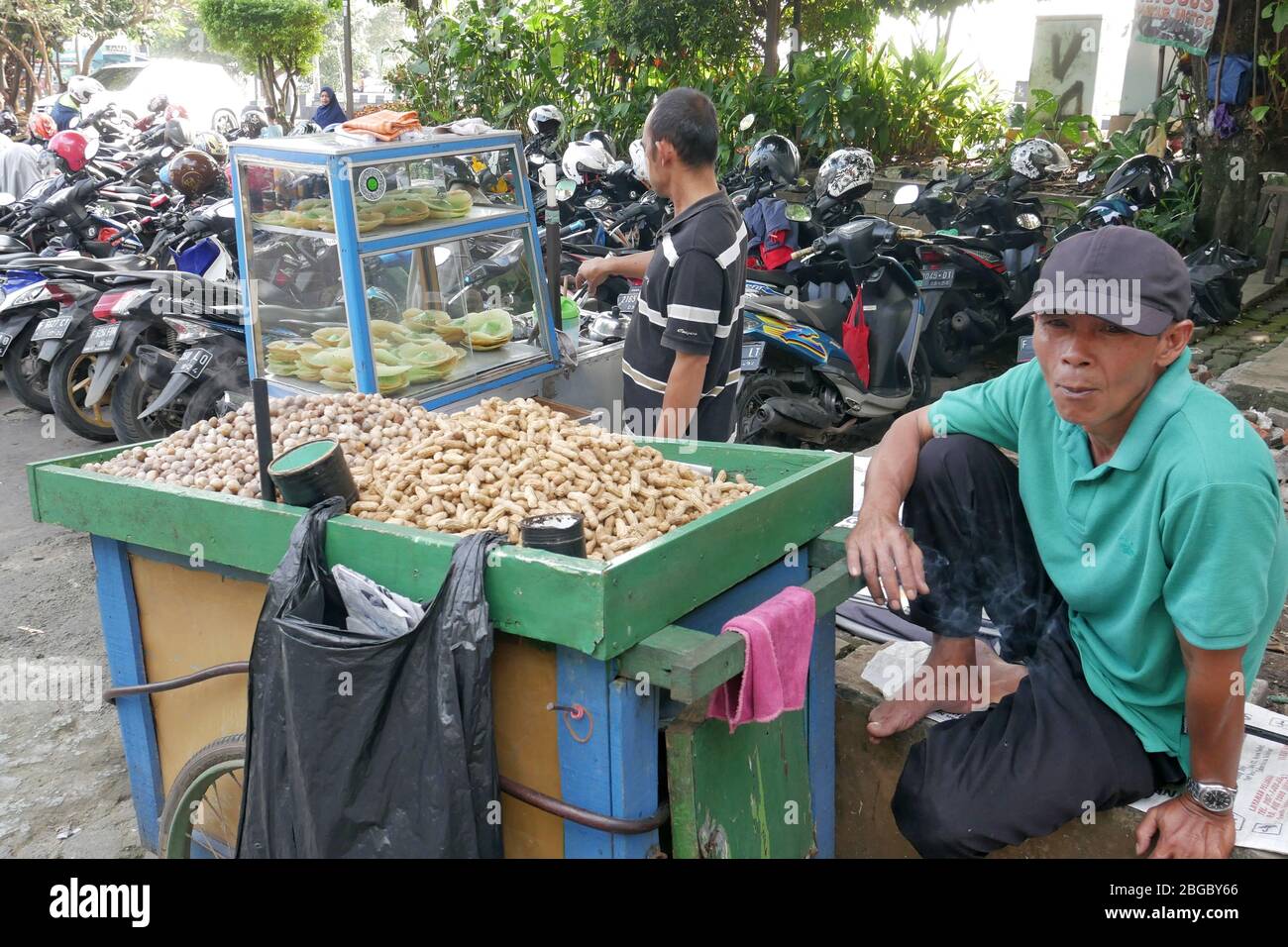 Un vendeur d'arachides bouillies attend les acheteurs à côté d'un parking de motos. Banque D'Images