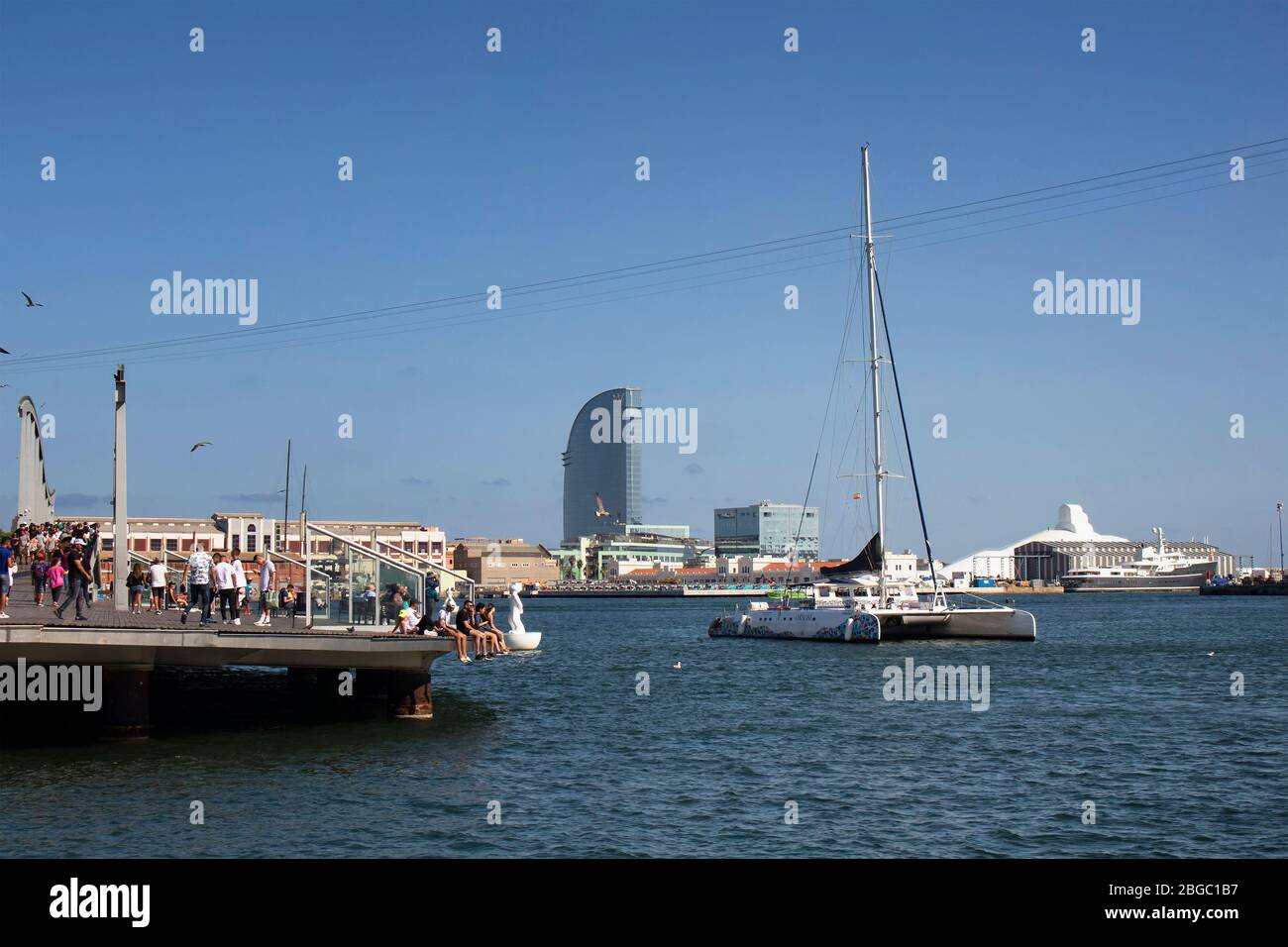 Vue sur le catamaran et les gens qui traînaient au port de Barcelone. C'est une journée d'été ensoleillée. Banque D'Images