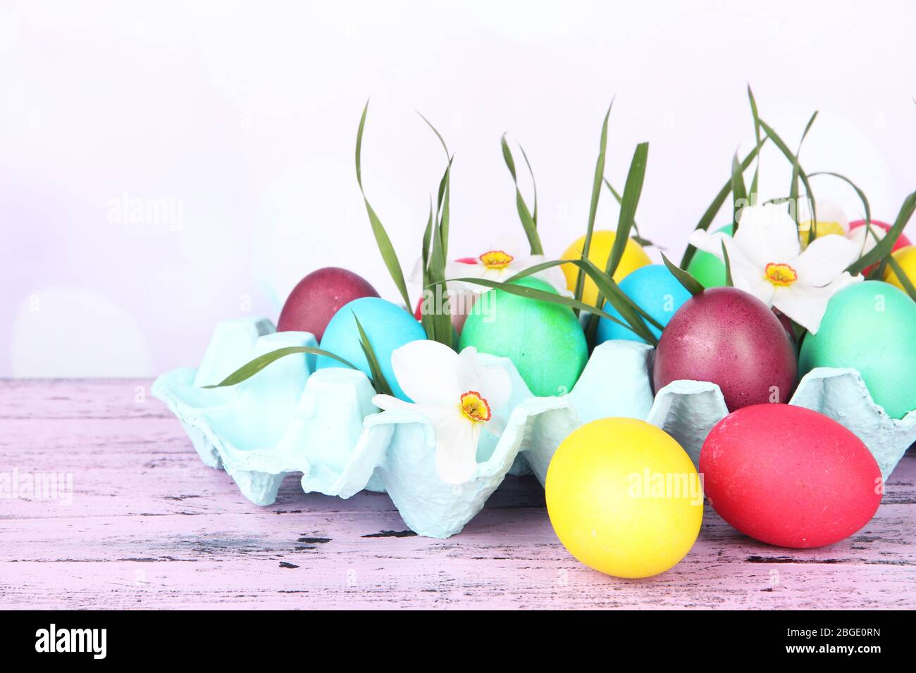 Oeufs de Pâques colorés avec herbe et fleurs dans le plateau sur la table sur fond clair Banque D'Images