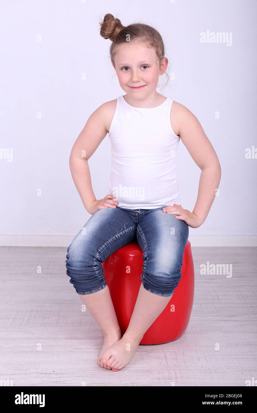 Belle petite fille assise sur un repose-pied en cuir sur fond de mur Banque D'Images