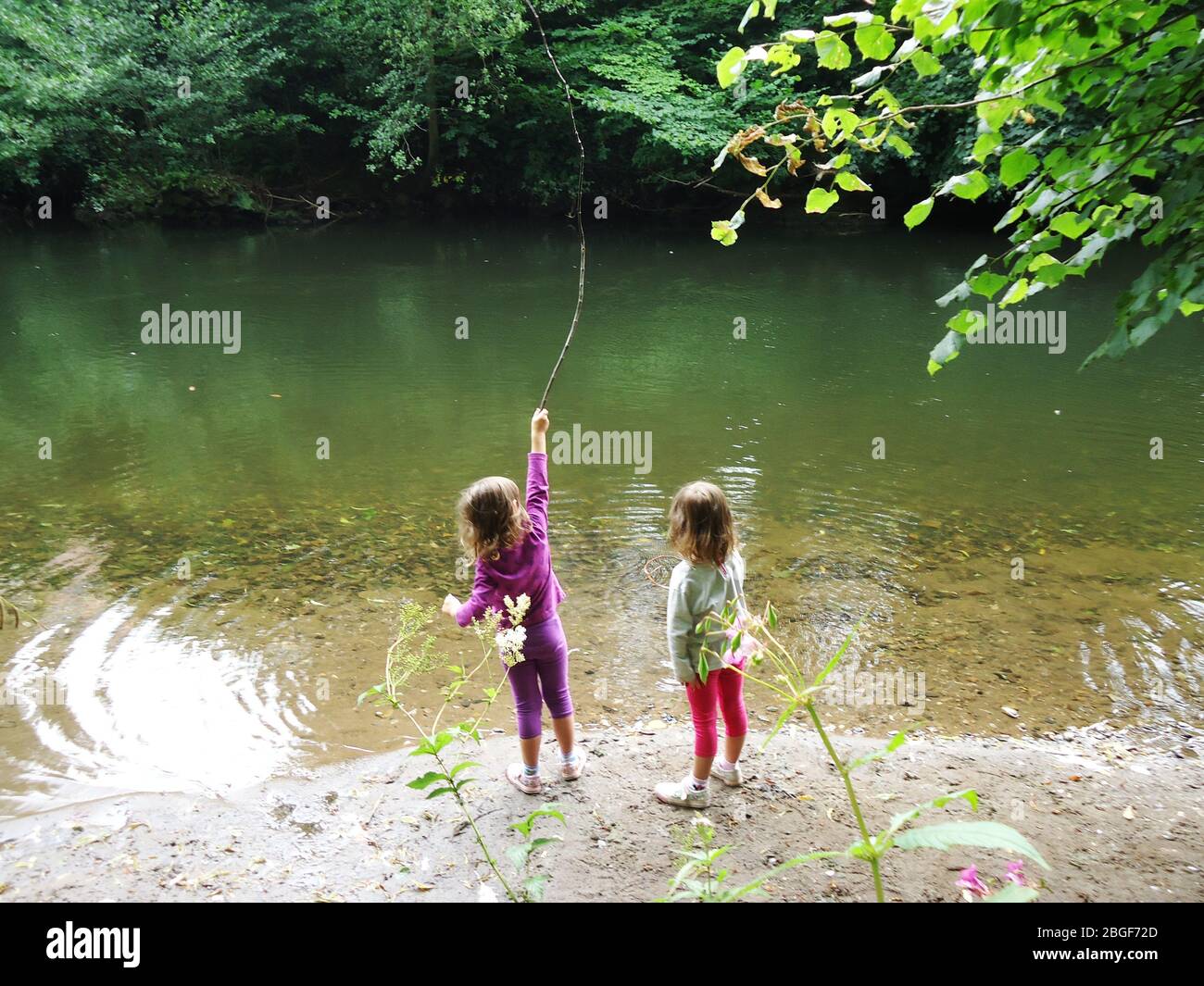 Jeunes filles jumelles jouant au bord de la rivière pendant une promenade dans le Derbyshire, Angleterre Banque D'Images