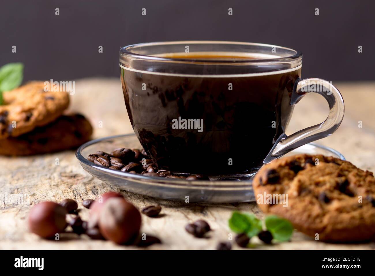 Café noir dans une tasse de verre avec des grains de café. Près des cookies et des noisettes Banque D'Images