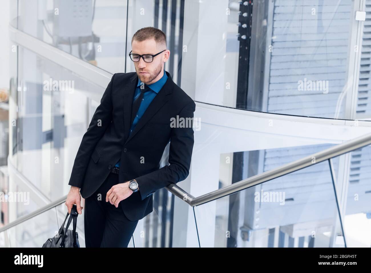 Photo de haut-angle d'un homme mûr et élégant en tenue de cérémonie. Il monte les escaliers avec le téléphone et la valise entre les mains. Banque D'Images