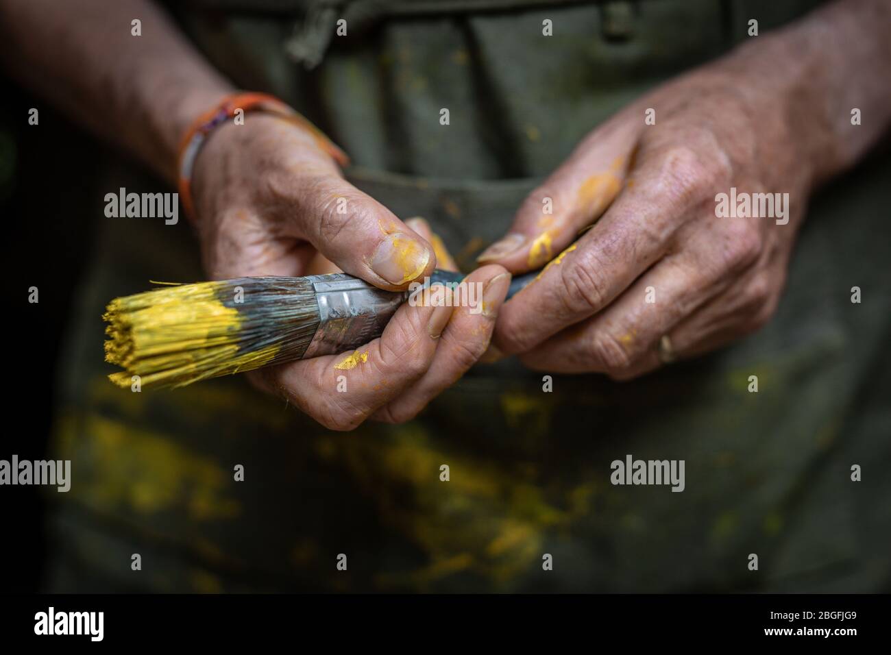 Gros plan des mains de peintre senior tenant un pinceau de peinture jaune. Banque D'Images