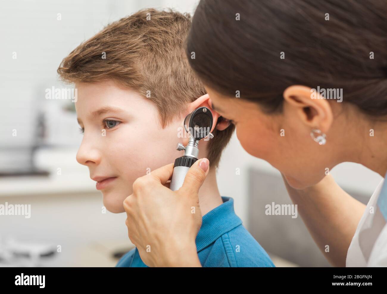 médecin examinant l'oreille de garçon, en utilisant l'otoscope, dans le bureau de médecins. Enfant soumis à un test auditif Banque D'Images