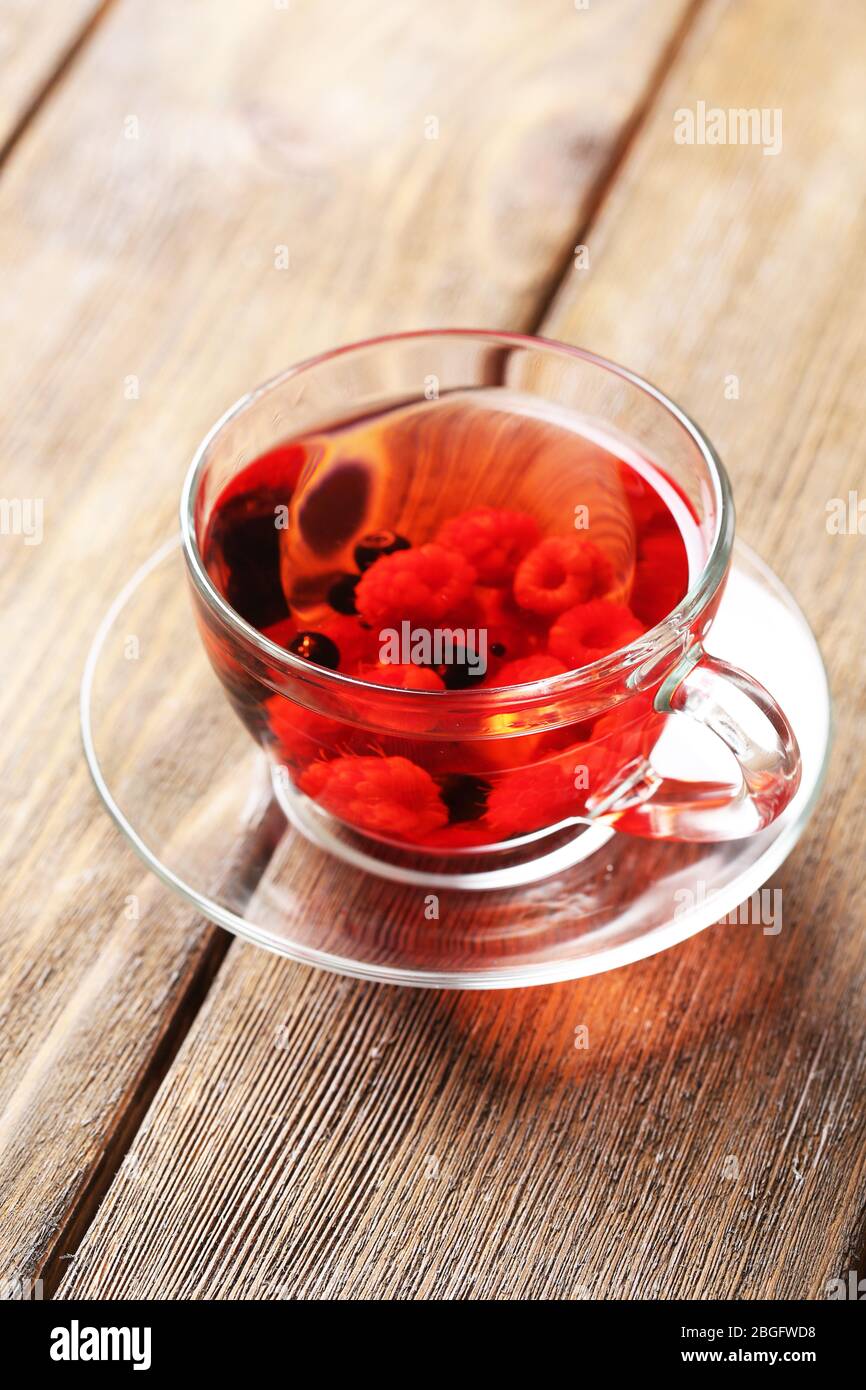 Thé rouge aux fruits avec baies sauvages dans une tasse en verre, sur fond en bois Banque D'Images