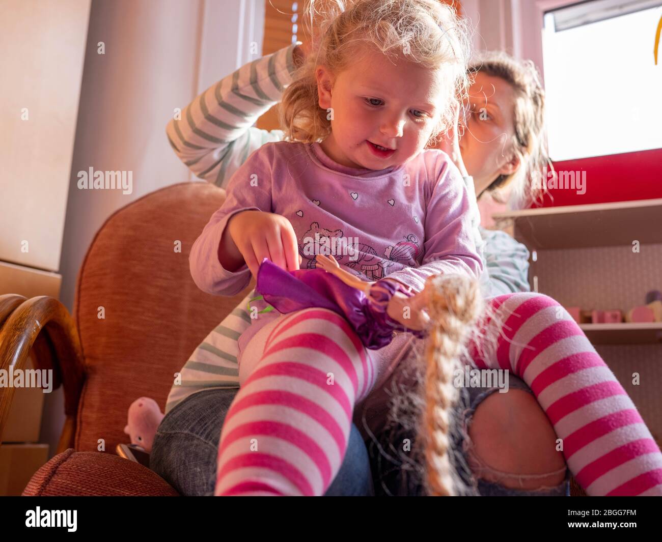 Une fille de deux ans (presque trois) est vérifiée pour les poux de tête par sa mère. Elle tient une poupée de Rainnzel Banque D'Images