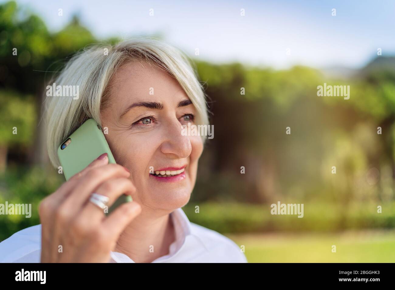 Femme âgée souriante parlant sur téléphone mobile tout en se reposant au parc Banque D'Images