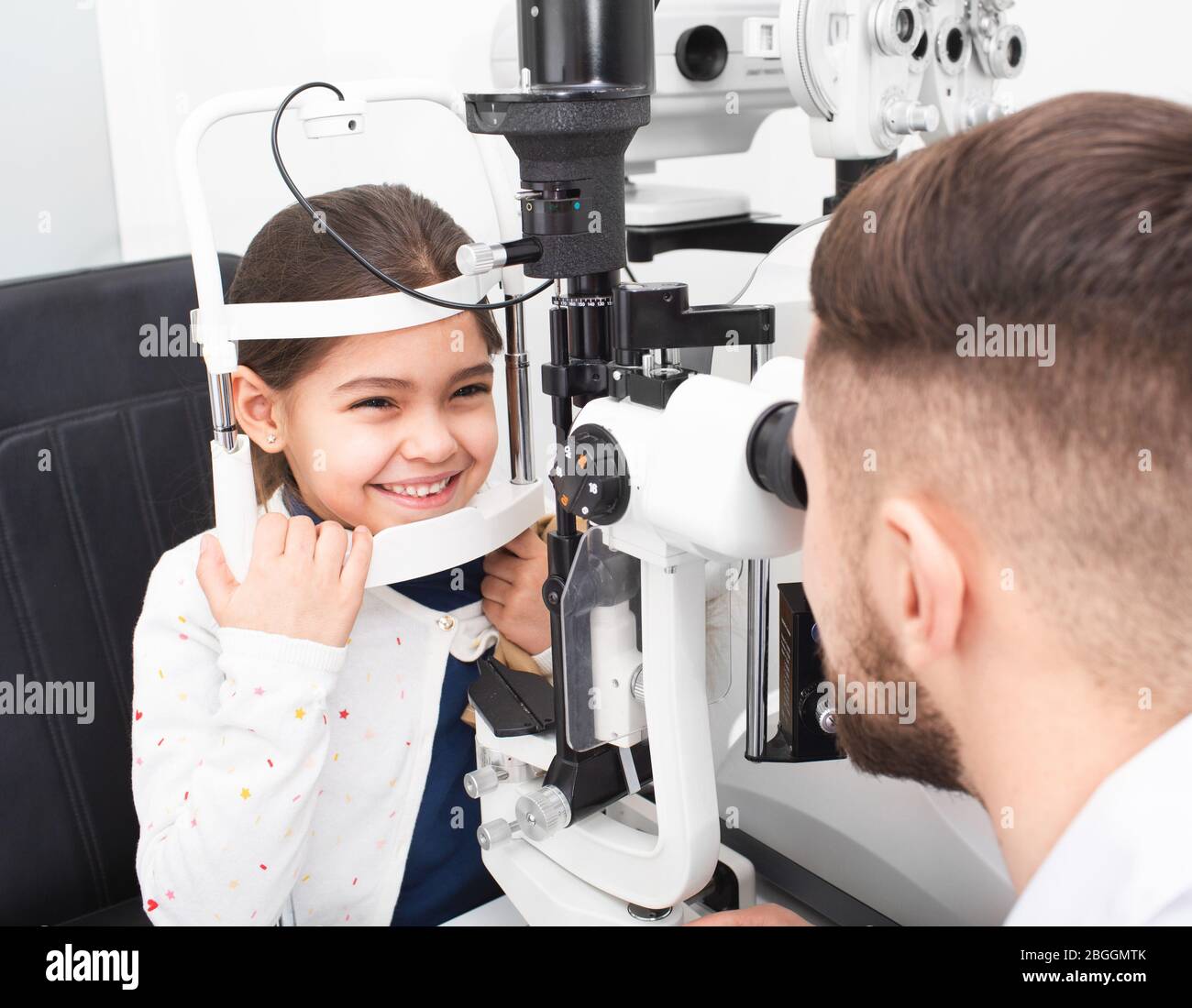 L'ophtalmologiste mâle vérifie la vue d'une petite fille à l'aide d'une lampe à fente binoculaire. Fille souriait parce que sa vue est très bonne Banque D'Images